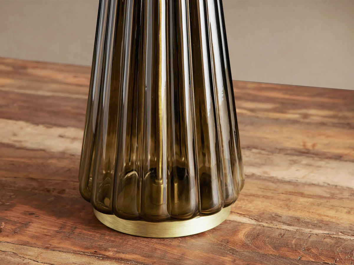 Elisabetta Table Lamp with a dark fluted glass conical base, brass-finish bottom, and white linen shade on a wood table.