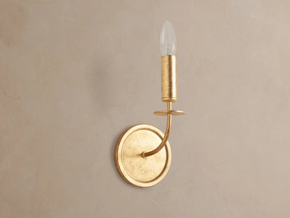 Arnett Sconce: antiqued gold leaf iron sconce with round backplate, curved arm, and candle-style holder with clear bulb.