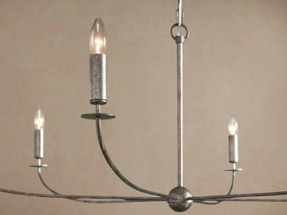 Arnett Round Chandelier with antiqued leaf finish, six candle-style lights, hanging by a chain against a beige wall.