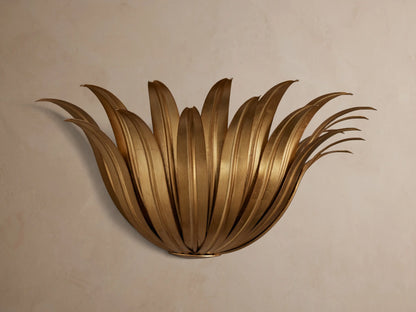 Matilde Sconce, an antique-gold iron wall light fixture with fanned, layered leaves, mounted on a light beige wall.