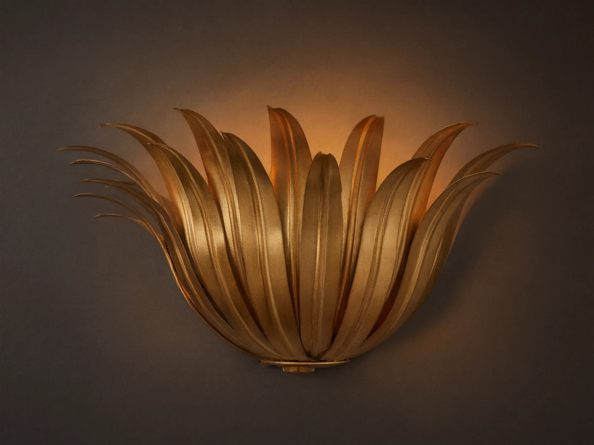 Matilde Sconce, an antique-gold iron wall light resembling layered leaves, casting a warm glow on a neutral wall.