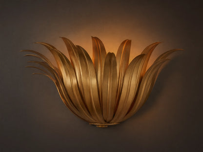 Matilde Sconce, an antique-gold iron wall light resembling layered leaves, casting a warm glow on a neutral wall.