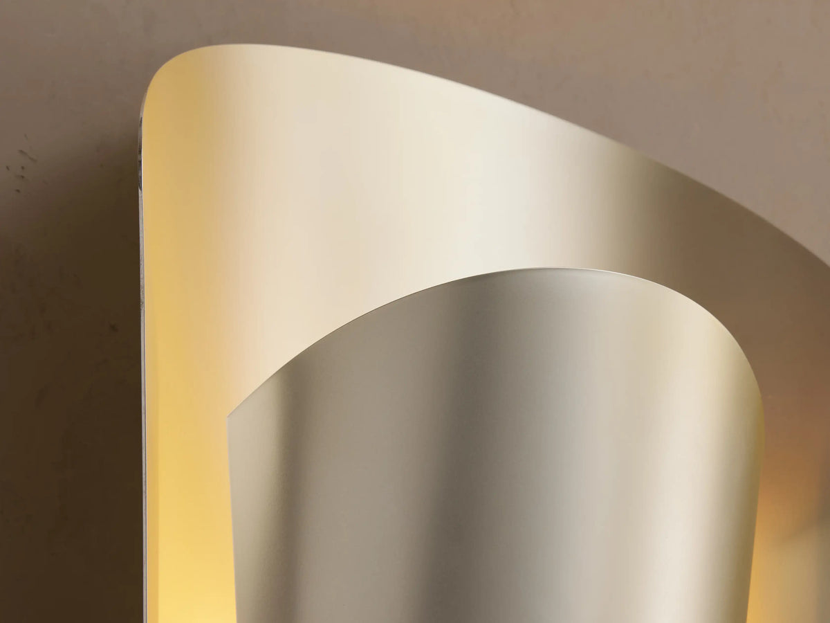 Strato Sconce: Elegant, vertically curved brass wall sconce with layered design & subtle metallic sheen, casting a warm glow on a beige wall.