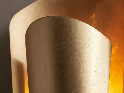 Strato Sconce, a vertical, curved gold brass wall sconce with a hand-applied leafed finish, mounted on a neutral wall.