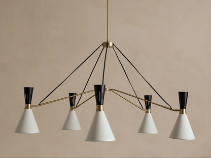 Ramsey Round Chandelier with five glowing white fabric conical shades, black accents, and brass arms on a beige wall.