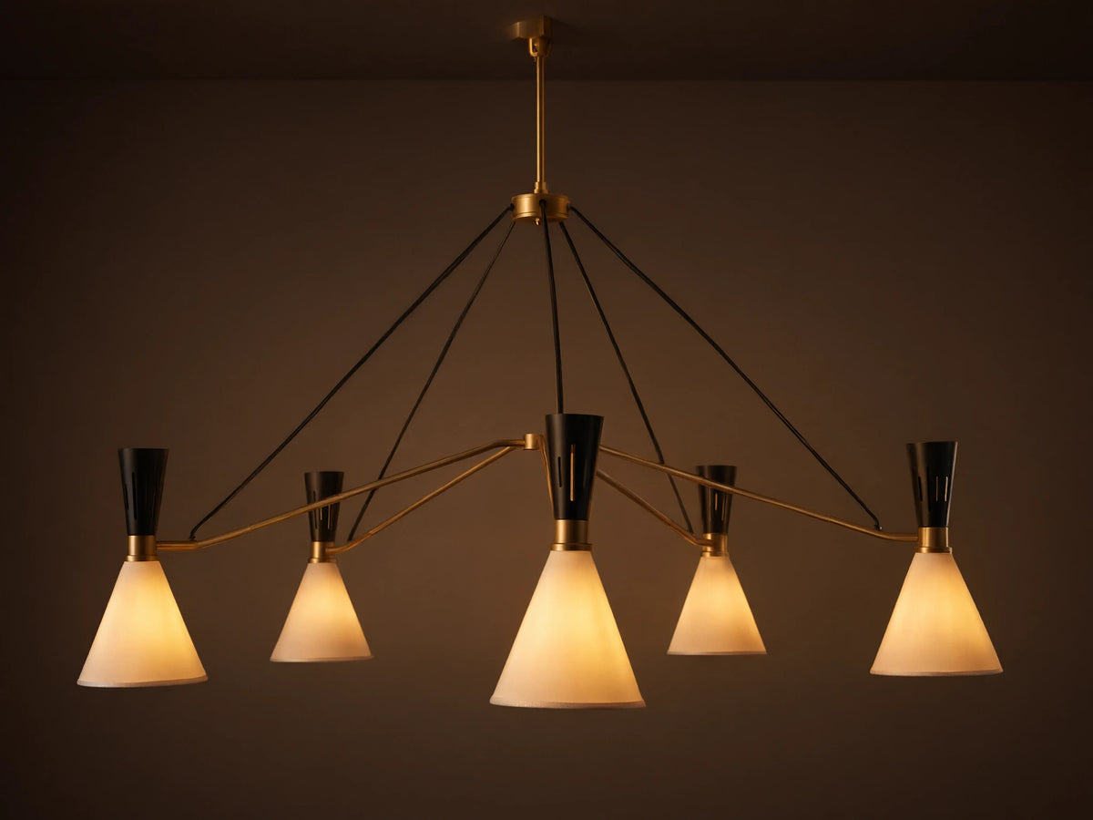Ramsey Round Chandelier with five glowing white fabric conical shades, black accents, and brass arms on a beige wall.