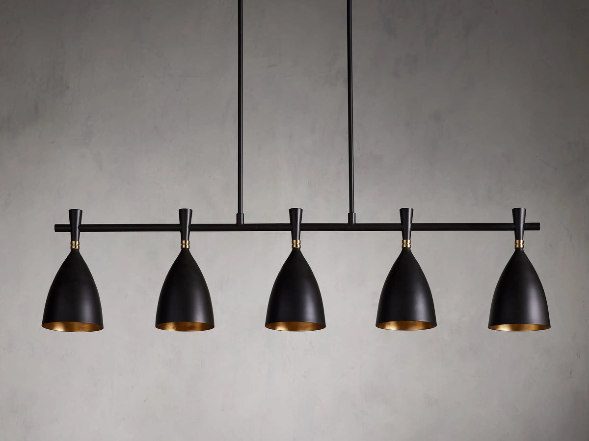 Jacarra Linear Chandelier with five black metal shades, gold leaf interior, hanging from an old bronze rod against a gray background.