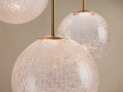 Close-up of Casen Round Chandelier with multiple illuminated crackle glass globes and satin brass rods against a light background.