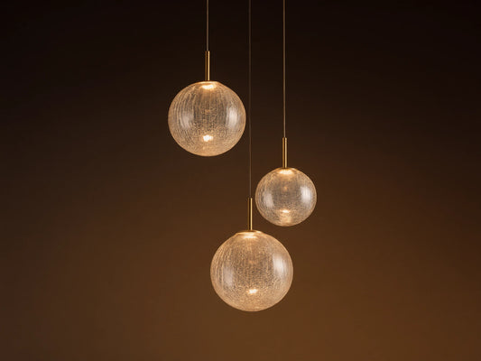 Casen Round Chandelier. Three illuminated crackle glass globes with satin brass accents, suspended at varying heights.