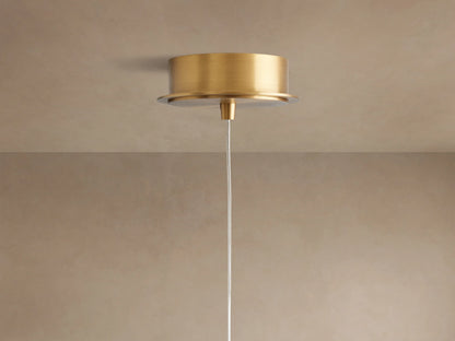 Close-up of Casen Pendant showing a glowing white opal glass globe with a satin brass stem and cap against a light wall.