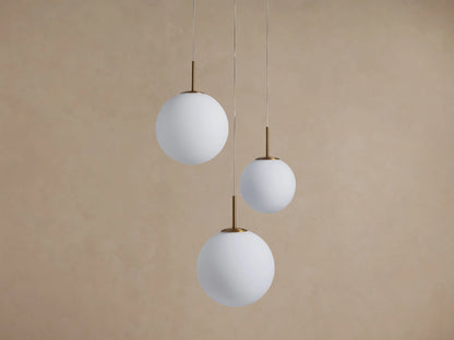 Casen Round Chandelier: Three white opal glass globes with satin brass stems, suspended at varying heights against a beige wall.