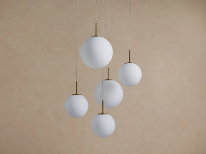 Casen Round Chandelier with five white opal glass globes and satin brass accents, hanging in a staggered arrangement.