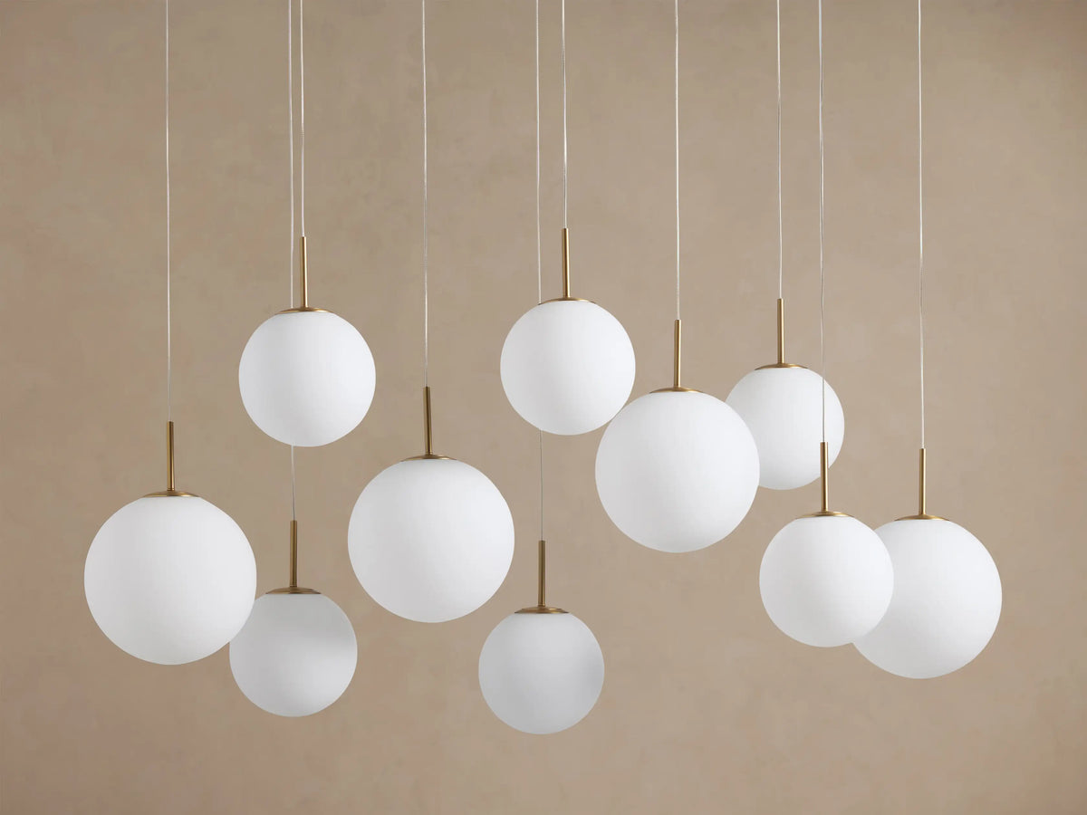 Casen Linear Chandelier, 10 glowing white opal glass globes with satin brass fittings, suspended at varying heights.