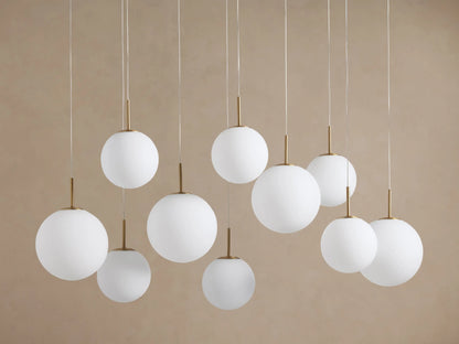 Casen Linear Chandelier, 10 glowing white opal glass globes with satin brass fittings, suspended at varying heights.