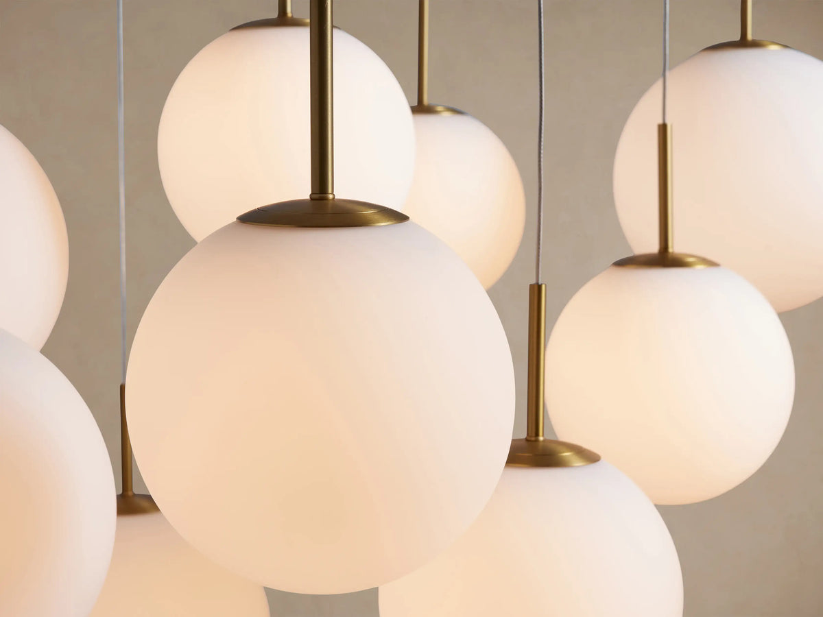 Close-up of a Casen Round Chandelier: glowing white opal glass globes suspended by satin brass rods.