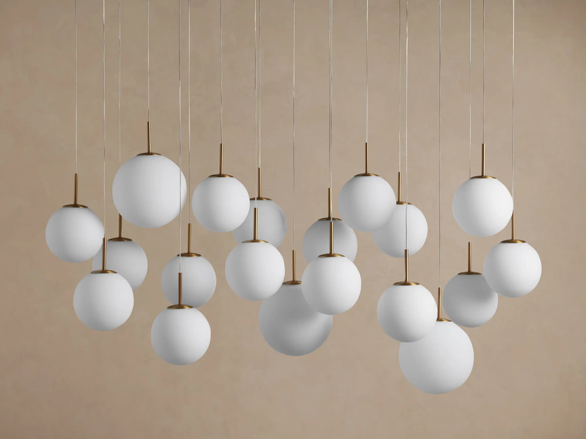 Elegant Casen Linear Chandelier: numerous glowing white opal globes with brass accents hang at varying lengths against a grey background.