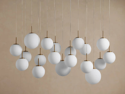 Elegant Casen Linear Chandelier: numerous glowing white opal globes with brass accents hang at varying lengths against a grey background.