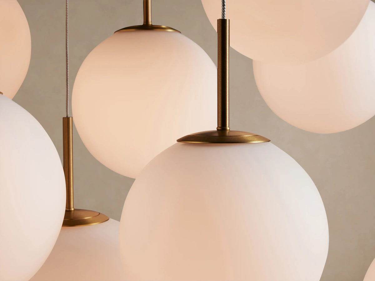 Casen Linear Chandelier with multiple white spherical opal glass globes hanging at varying heights from satin brass fixtures.