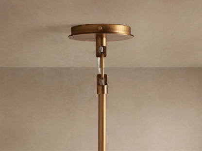 Close-up of the Adria 2-Light Chandelier, showing its brushed brass arm and illuminated pleated white shade with a warm glow.