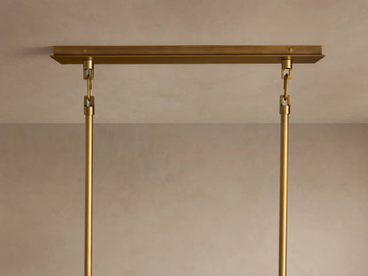 Close-up of Adria Linear Chandelier. Brass frame supports four glowing, light-colored fabric shades with matching brass trim.