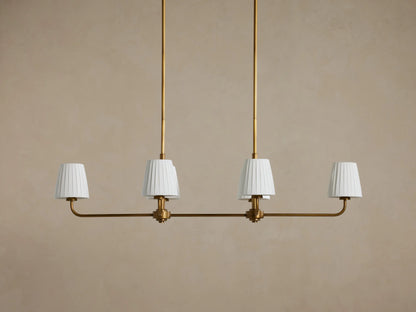 Adria Linear Chandelier with 4 illuminated pleated white shades on a horizontal brass bar, hanging from 2 brass rods.