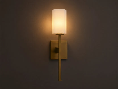 Cinda Sconce, a vertical brass finish wall light with a glowing rectangular stone shade, mounted on a tan wall next to a mirror.