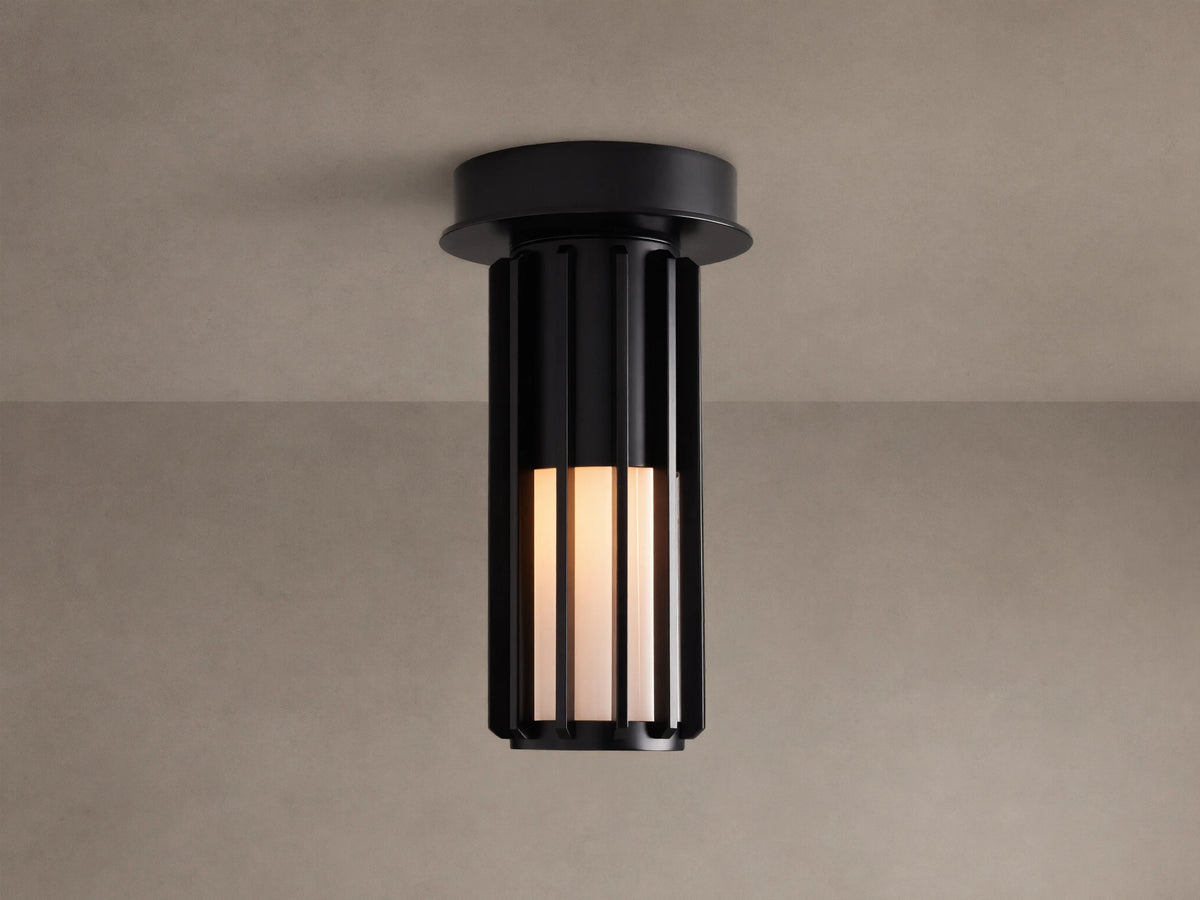 Matte black Gabbia Outdoor Spotlight Flush Mount, cylindrical with vertical slats, flush-mounted to a light brown ceiling. Inner milk glass panels glow.