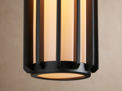 Matte black Gabbia Outdoor Sconce with a rectangular backplate, cylindrical ribbed body, and white milk glass, on a beige wall.