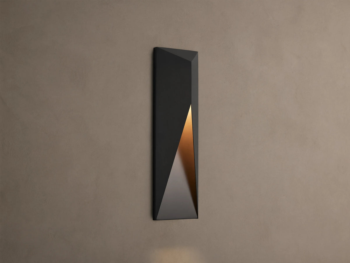 Modern dark grey Davian Outdoor Sconce, vertically mounted, with geometric facets and warm bronze light emanating from inside.