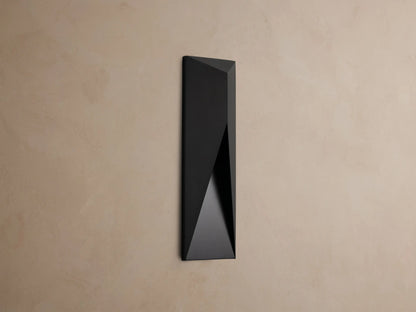 Modern dark grey Davian Outdoor Sconce, vertically mounted, with geometric facets and warm bronze light emanating from inside.