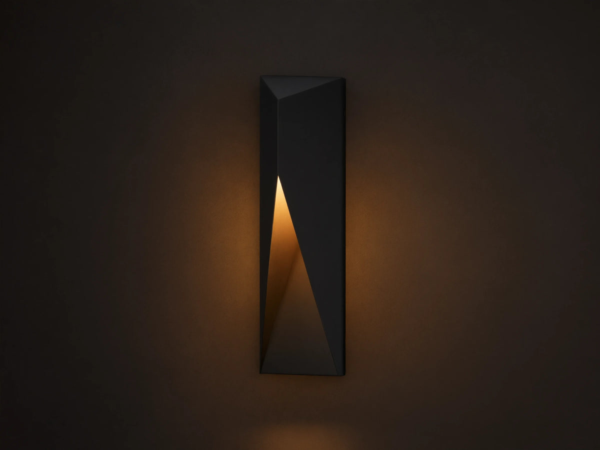 Modern dark grey Davian Outdoor Sconce, vertically mounted, with geometric facets and warm bronze light emanating from inside.
