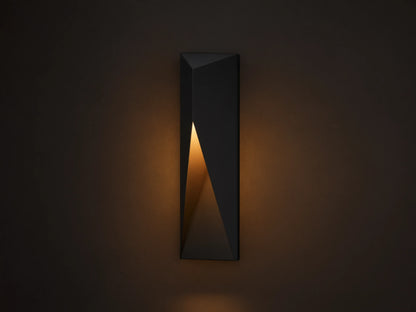 Modern dark grey Davian Outdoor Sconce, vertically mounted, with geometric facets and warm bronze light emanating from inside.