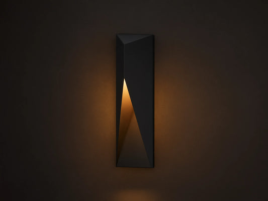 Modern dark grey Davian Outdoor Sconce, vertically mounted, with geometric facets and warm bronze light emanating from inside.