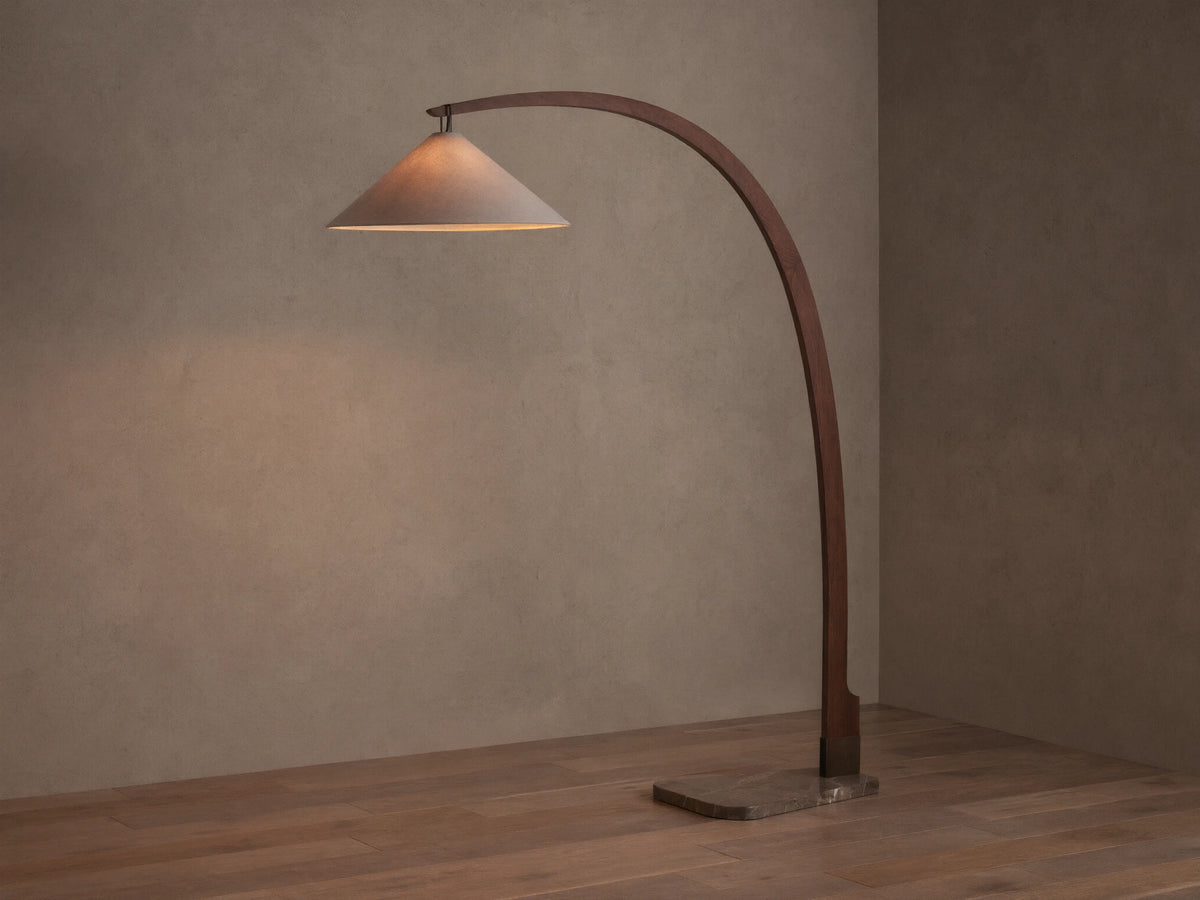 Monviso Floor Lamp with curved walnut wood frame, espresso stone base, and glowing white fabric shade on a wooden floor.