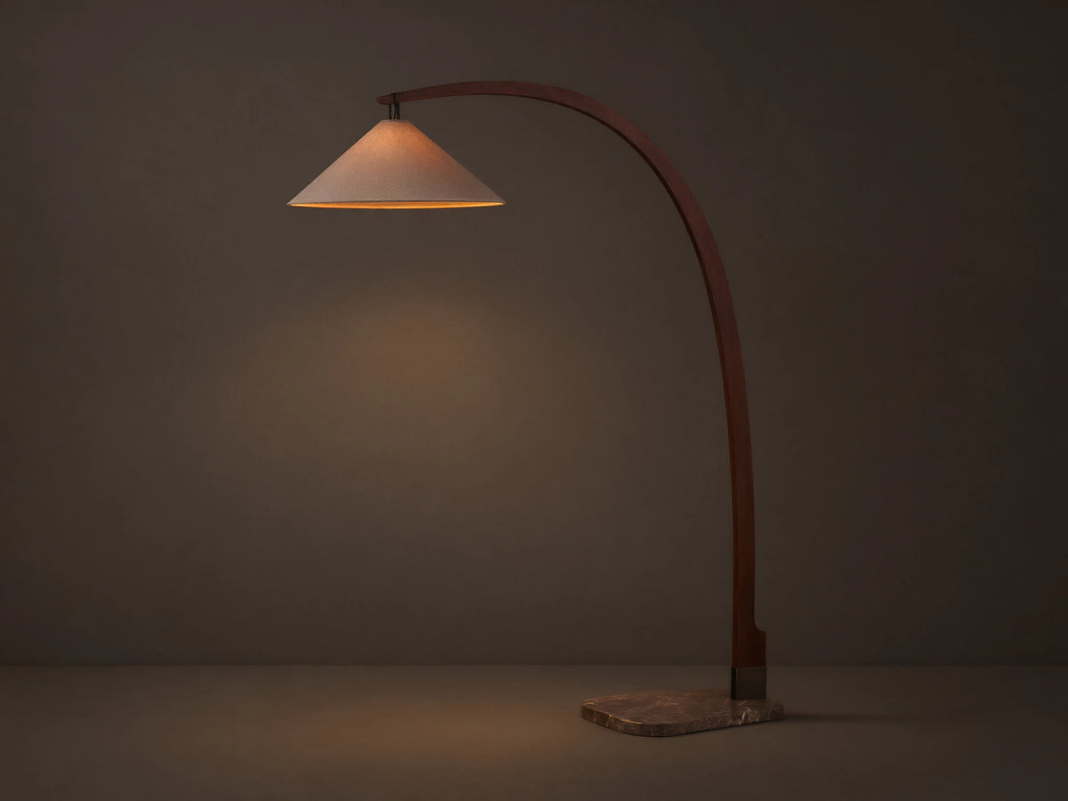 Monviso Floor Lamp with curved walnut wood frame, espresso stone base, and glowing white fabric shade on a wooden floor.