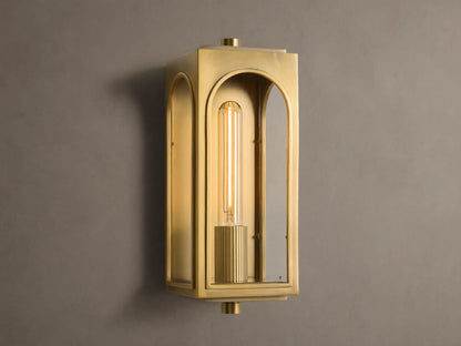 Palladian Outdoor Sconce: Polished brass rectangular fixture with arched glass, bright tubular bulb, mounted on a grey wall.