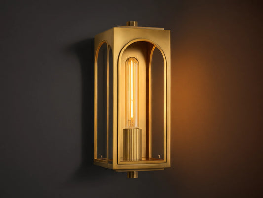 Palladian Outdoor Sconce: Polished brass rectangular fixture with arched glass, bright tubular bulb, mounted on a grey wall.