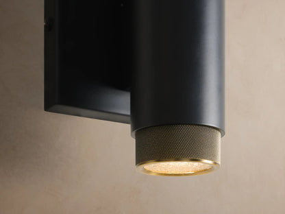 Matte black cylindrical Spotlight Outdoor Sconce with brass knurled ends, mounted horizontally on a light beige wall.