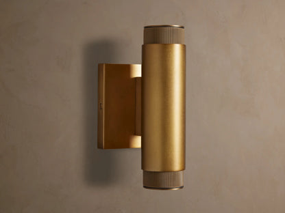 Vertical brass Spotlight Outdoor Sconce, cylindrical, mounted on a wall, with knurled end caps, emitting light up and down.