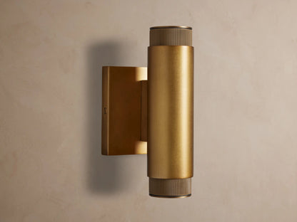 Vertical brass Spotlight Outdoor Sconce, cylindrical, mounted on a wall, with knurled end caps, emitting light up and down.