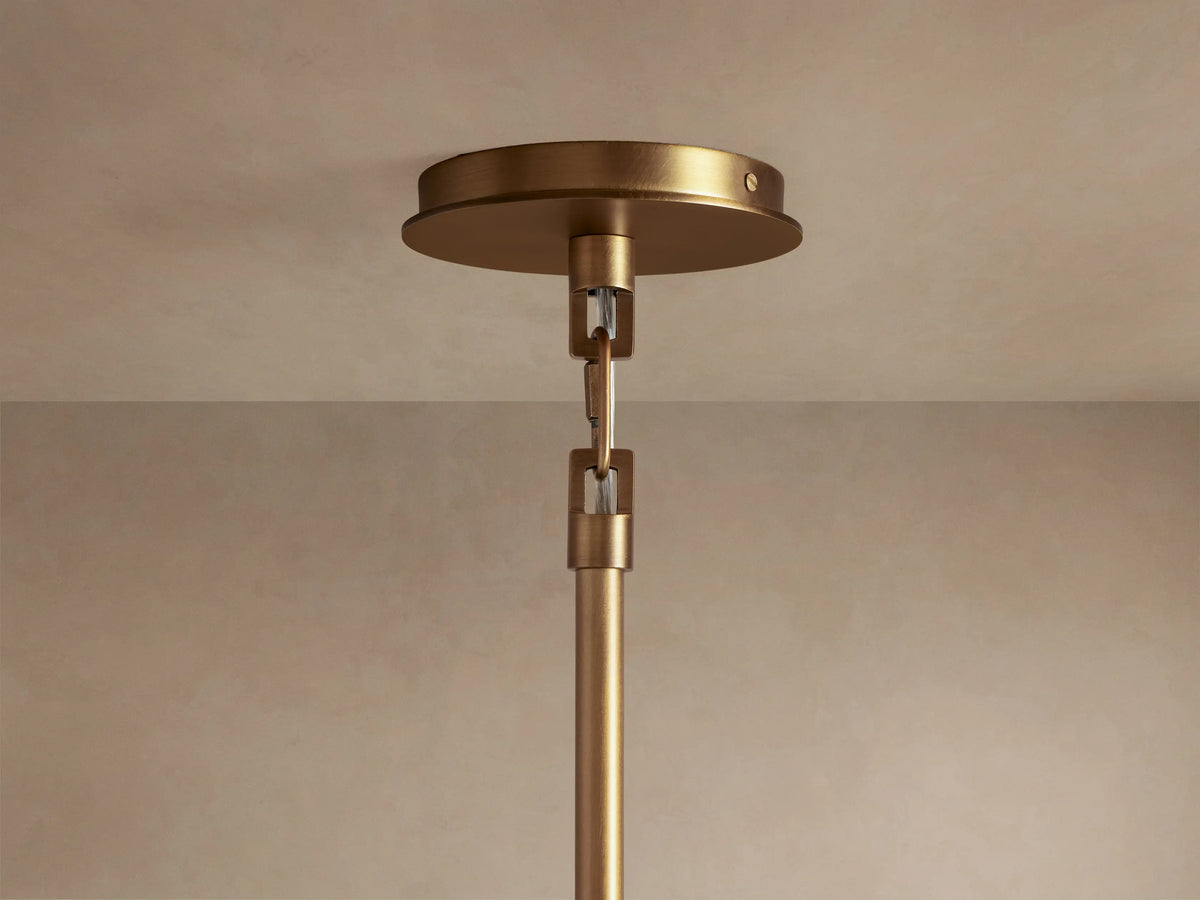 Close-up of the Adria Pendant's conical light beige fabric shade with an antique brass rim, emitting a warm glow from below.