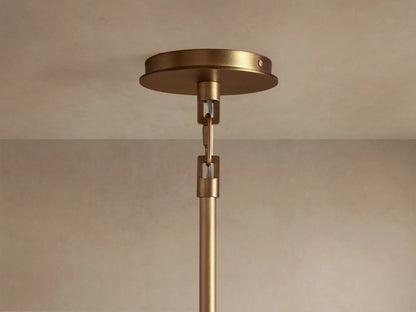 Close-up of the Adria Pendant's conical light beige fabric shade with an antique brass rim, emitting a warm glow from below.
