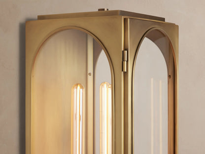 Brass Palladian Outdoor Sconce with a plated finish, clear arched glass, and a vertical linear bulb, mounted on a light wall.