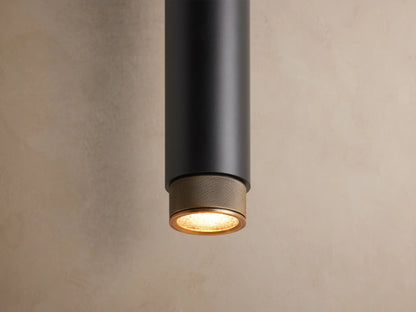 Matte black Spotlight Outdoor Sconce mounted vertically on a light brown wall, featuring brass knurled caps on each end.