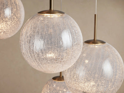 Casen Round Chandelier featuring multiple illuminated crackle glass globes suspended by satin brass rods against a light wall.
