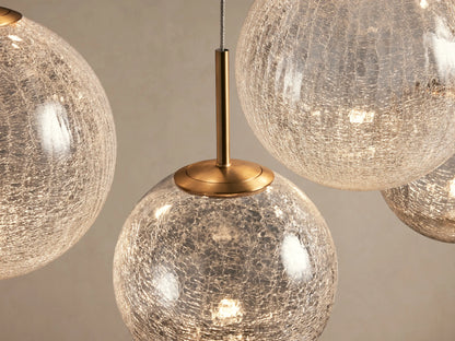 Casen Linear Chandelier with 10 crackle glass globes of varying sizes, suspended by thin wires from brass fittings against a beige wall.