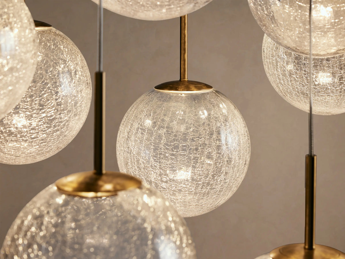 Casen Linear Chandelier featuring multiple clear, crackled glass globes suspended at varying heights with brass accents.