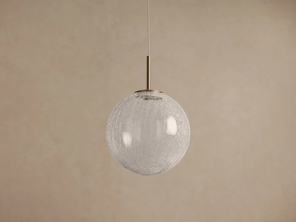 Casen Pendant with glowing, spherical crackle glass globe hanging from a brass rod against a textured brown wall.