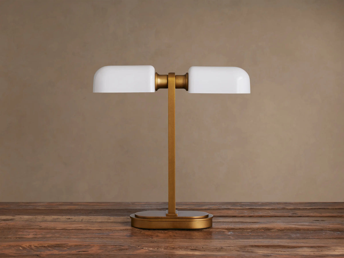Zayd Table Lamp: modern brass base and stem, supporting two glowing horizontal opal glass shades, on a dark wooden table.