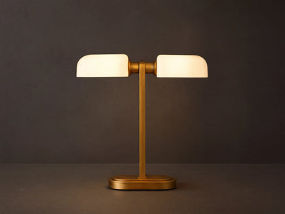 Zayd Table Lamp: modern brass base and stem, supporting two glowing horizontal opal glass shades, on a dark wooden table.